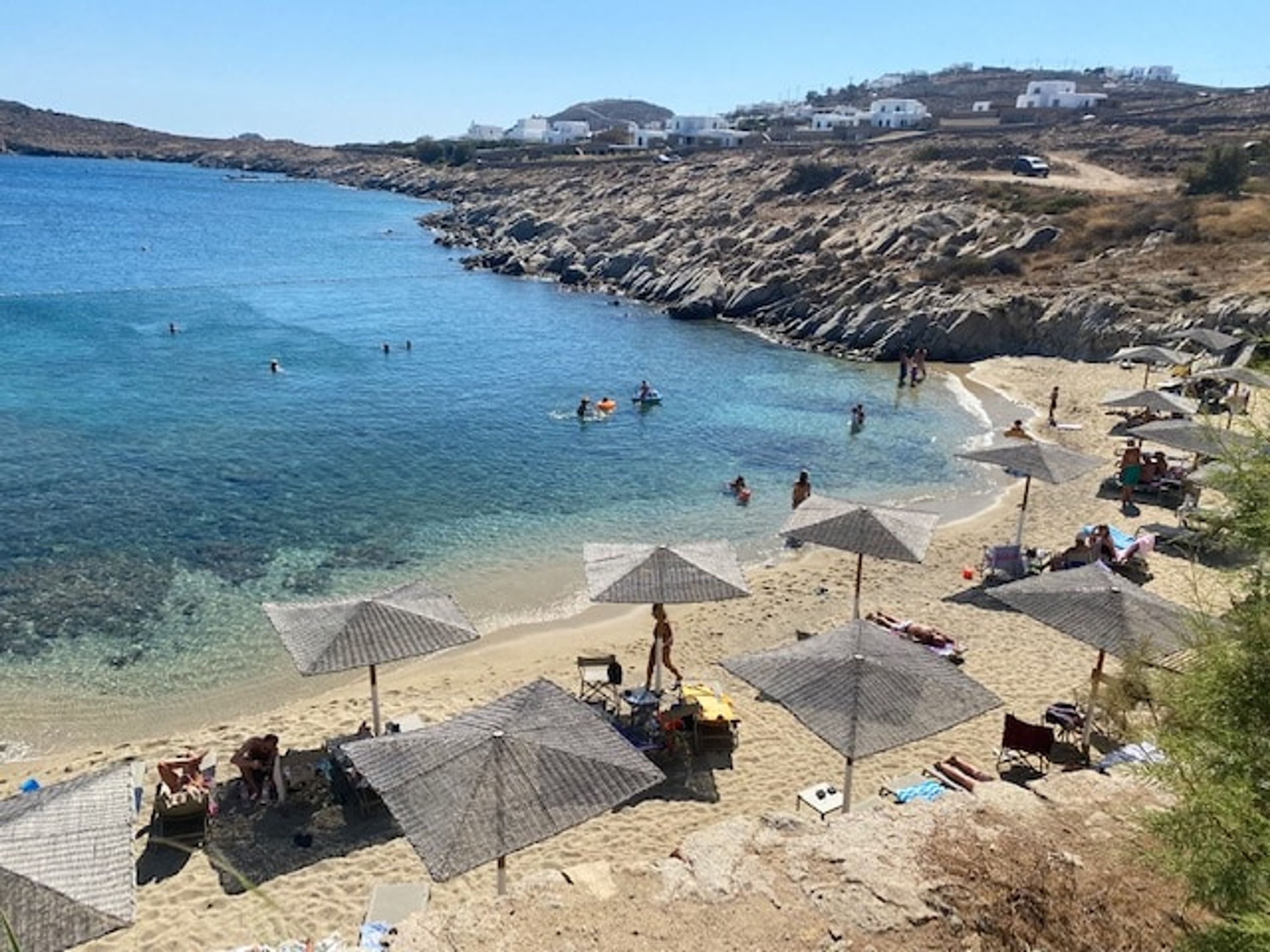 Una playa con agua azul cristalina, costa rocosa y varias sombrillas que dan sombra.