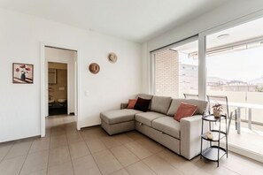 A modern living room with a sectional sofa, a small side table, and a view of the city through large windows. - Modern Comfort in Lugano (Mola Giglio) (Lugano)