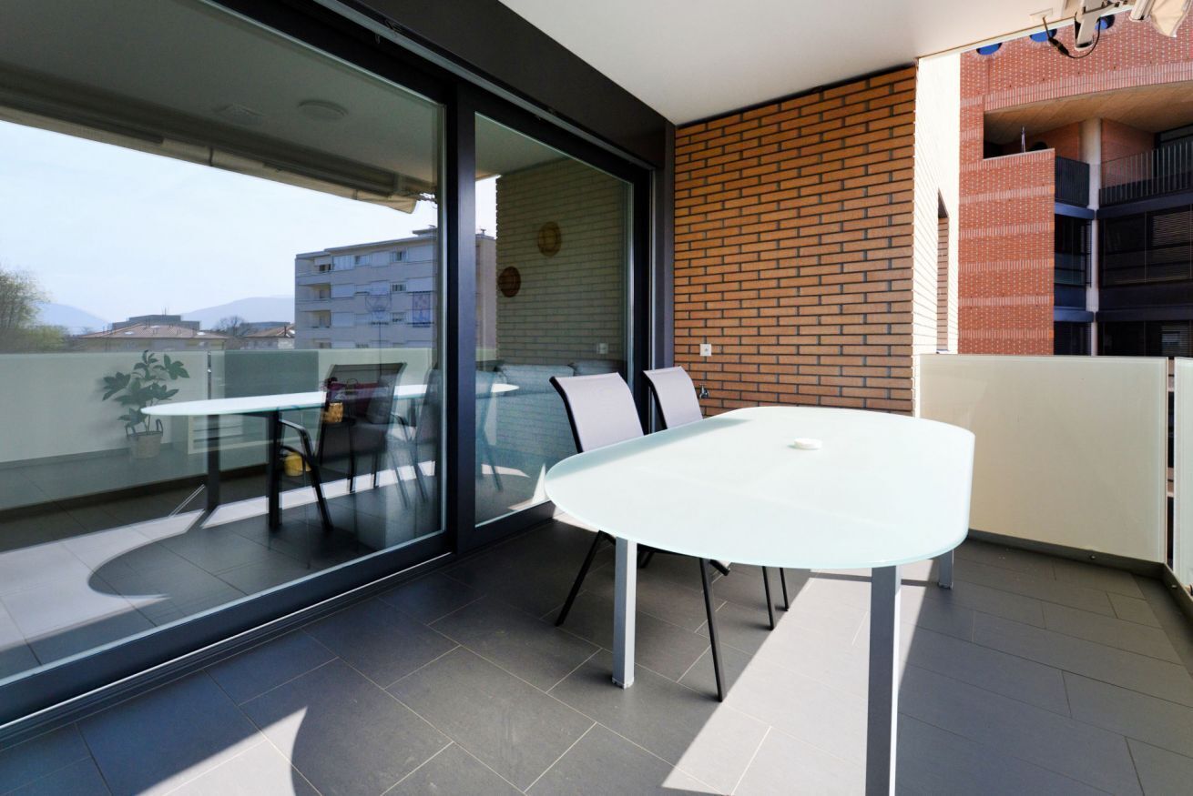 Un balcón moderno con puerta de cristal, una mesa blanca y pared de ladrillo.