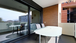 Ein moderner Balkon mit Glastür, weißem Tisch und Backsteinwand.