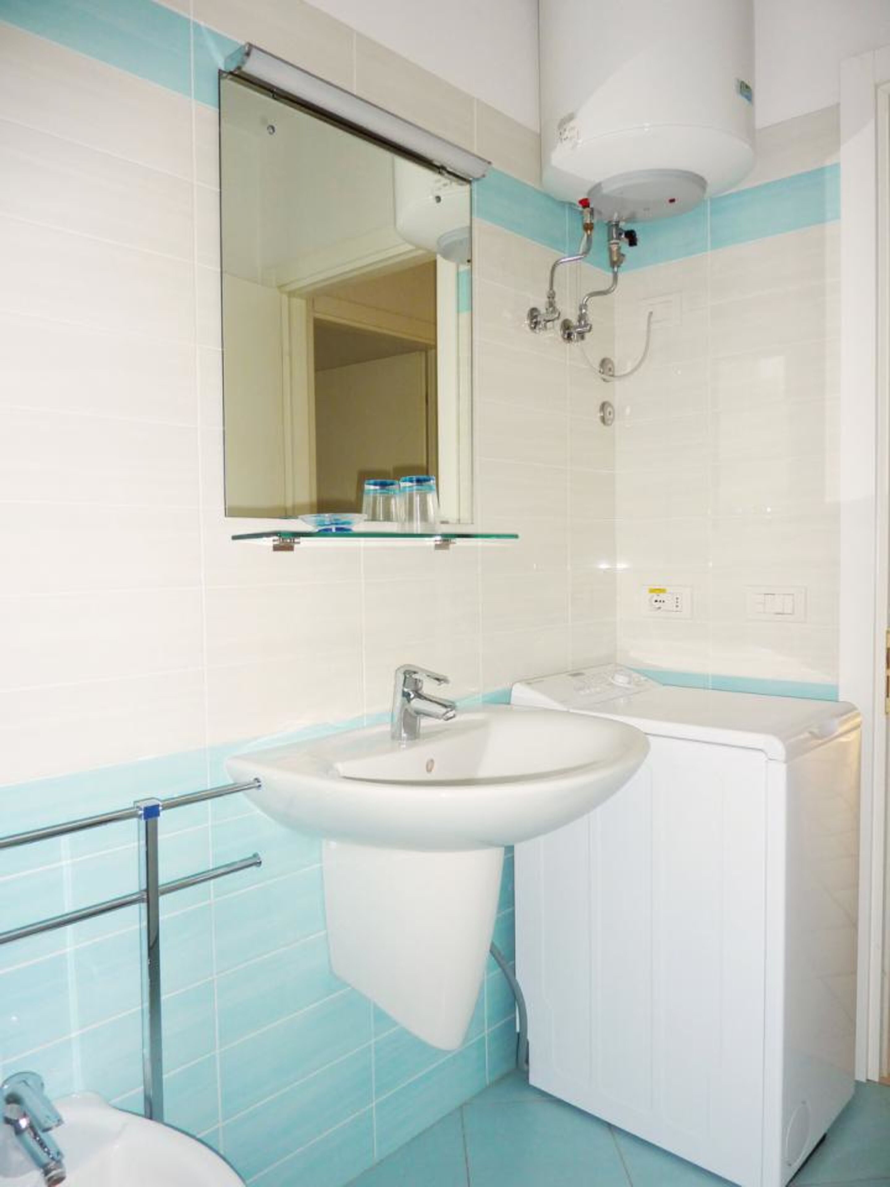 Un baño con lavamanos, espejo y lavadora.