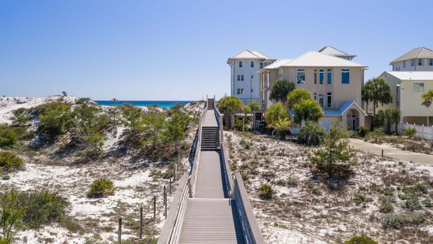 Un hotel sulla costa con una passerella in legno che conduce alla spiaggia, circondato da dune sabbiose e vegetazione rada.