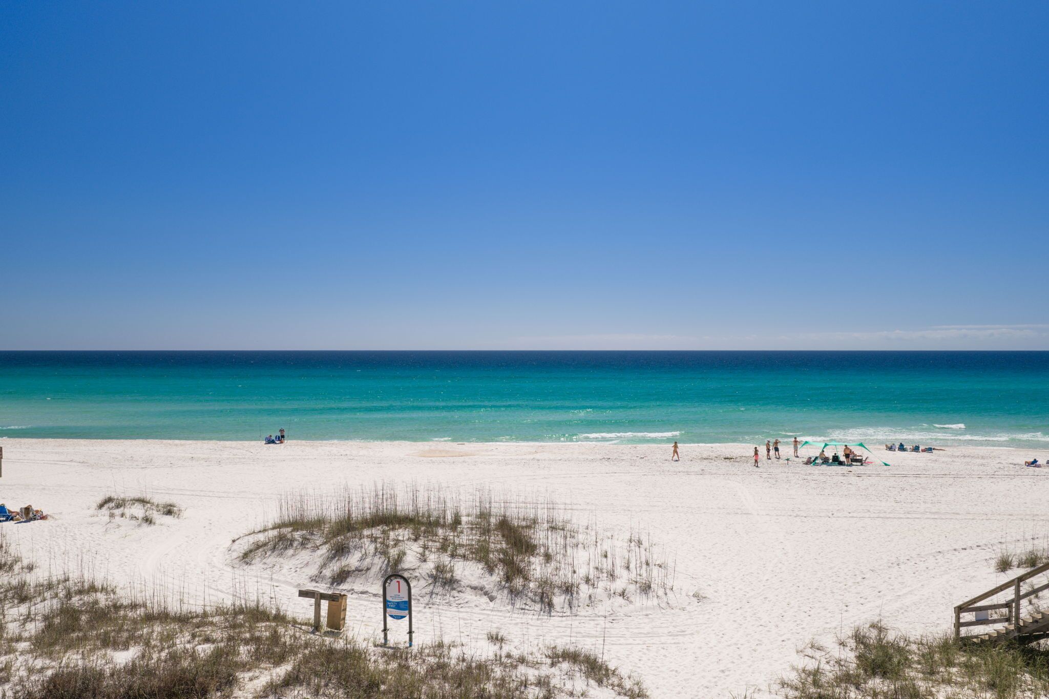 A beach with white sand, clear blue water, and a wooden walkway leading to a beach hut.