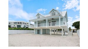 Een tweelaags strandhuis met een balkon, een overdekte veranda en een omheinde tuin.