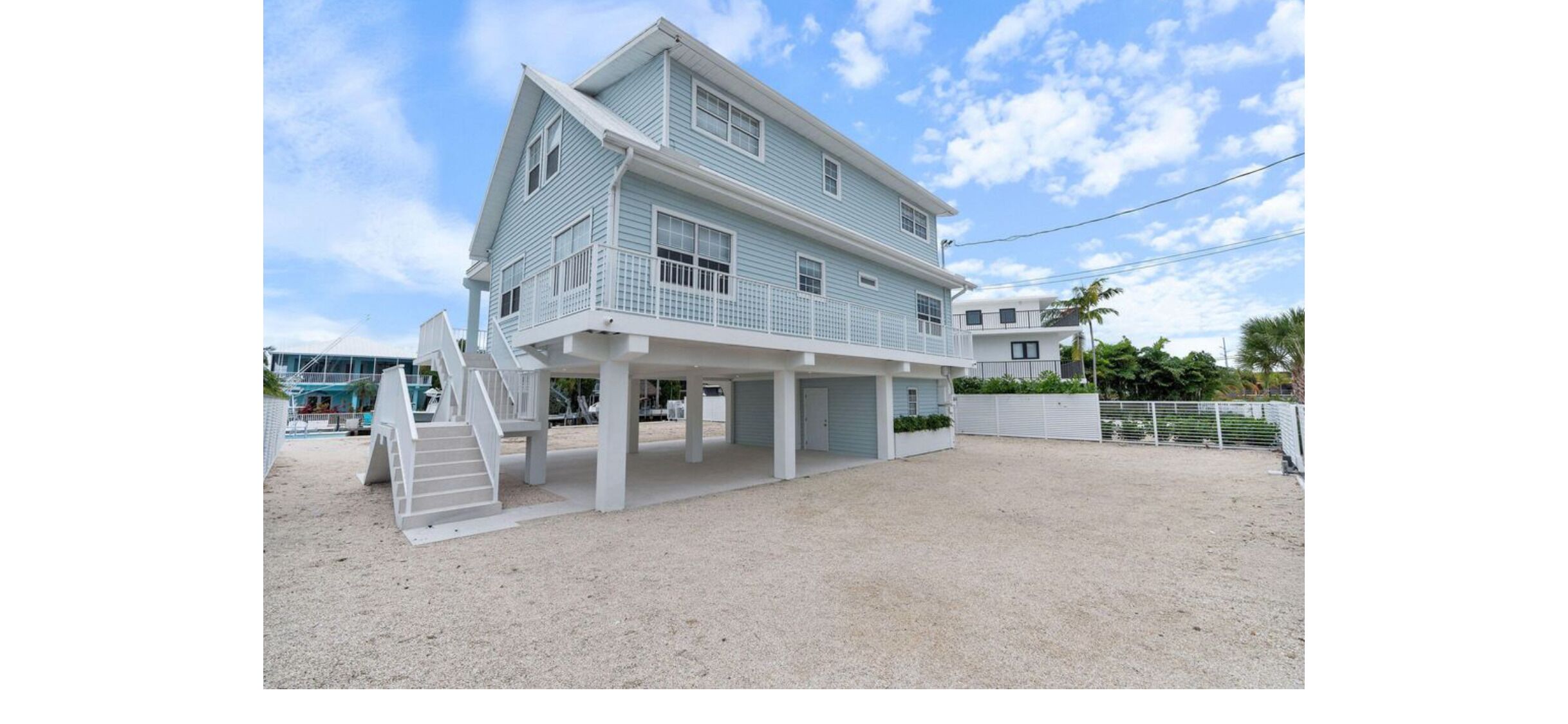 Een twee verdiepingen tellend strandhuis met een overdekt terras en een trap naar de bovenverdieping.