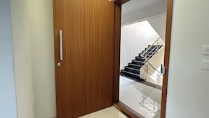 A hallway with a wooden door, a brown mat, and a view of a staircase leading to an upper floor.