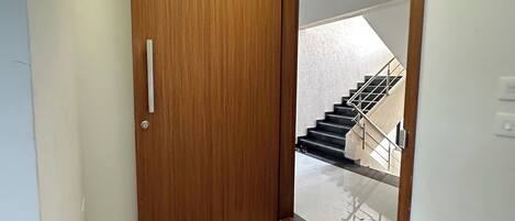 A hallway with a wooden door, a brown mat, and a view of a staircase leading to an upper floor.
