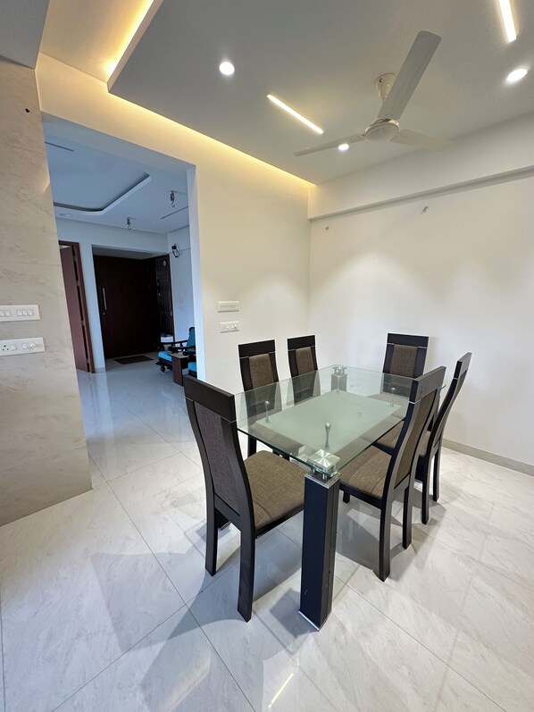 Un comedor moderno con una mesa de vidrio, seis sillas y un ventilador de techo.