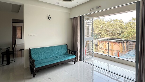 A spacious living room with a teal sofa, a ceiling fan, and a large sliding glass door leading to an outdoor balcony.