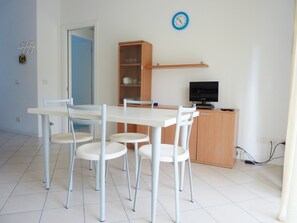 Ein Zimmer mit einem weißen Tisch und Stühlen, einem Holzschrank, einem Fernseher und einer Wanduhr.
