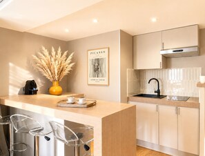 A modern kitchen with a central island, bar stools, a coffee machine, and a framed artwork on the wall. - 1532 Mouffetard (Paris)