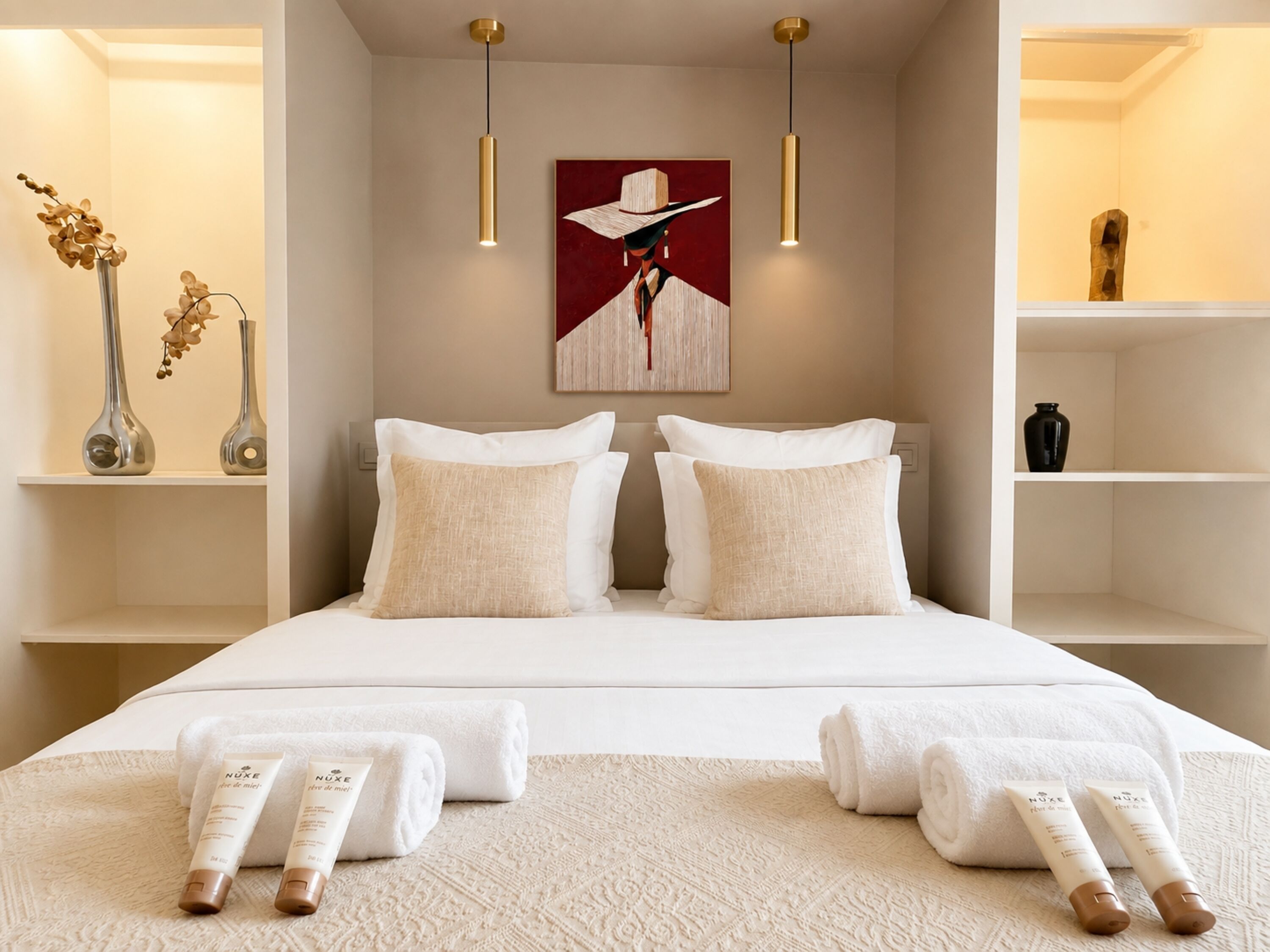 A hotel room with a bed, two bedside tables, a painting, and a shelf with decorative items.
