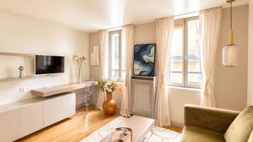 Una sala de estar moderna con un sofá, una mesa de centro, un televisor y un comedor con una silla y un jarrón de flores.