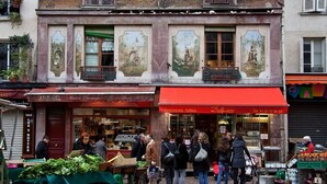A street scene with a building featuring large murals and a red awning with a restaurant sign. - 1532 Mouffetard (Paris)
