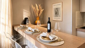 Un comedor con una mesa de madera preparada para dos personas, una botella de vino y un cuadro en la pared.