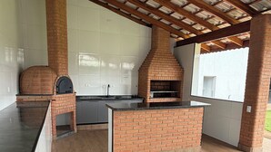 Ein Außenbereich mit Küche, einschließlich eines Backofens aus Ziegelsteinen und eines Grills, unter einer Holzdachkonstruktion.