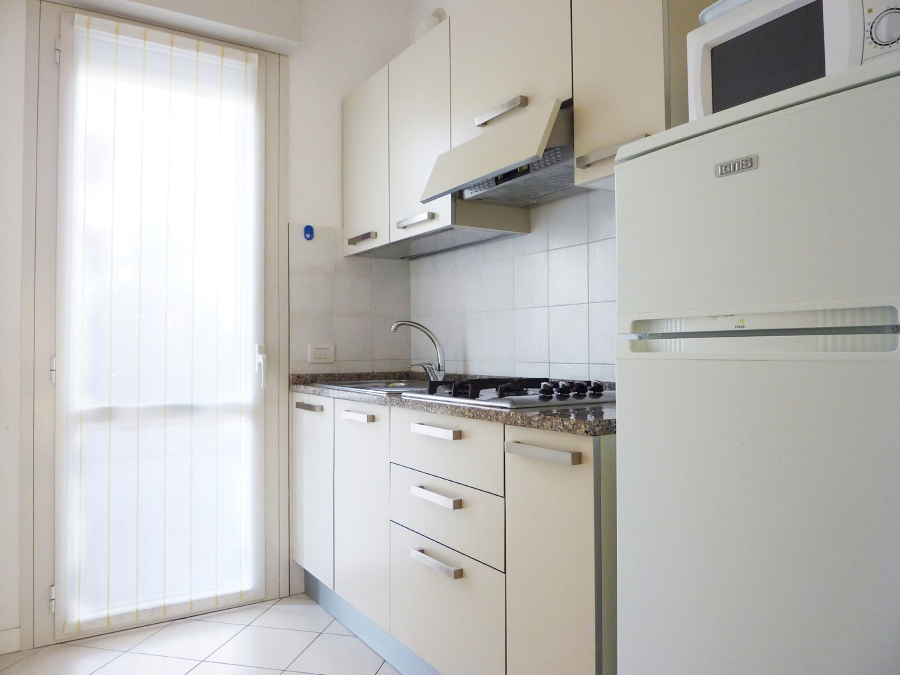 Una cucina con mobili bianchi, un fornello a gas, un forno a microonde e un lavello.