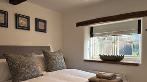 Een slaapkamer met een groot bed, gestreepte kussens, een raam met uitzicht en ingelijste foto's aan de muur.