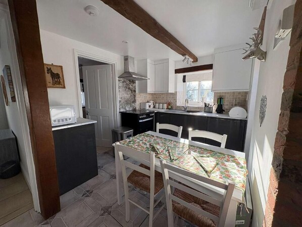 Una cocina compacta con armarios blancos, una isla central y una mesa de comedor con mantel floreado.