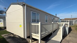 A mobile home with a front deck, a satellite dish, and a window with curtains. - Seaview 1. (Skegness)