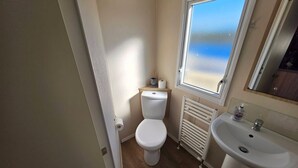 A bathroom with a toilet, a radiator, a sink, and a window with a view. - Seaview 1. (Skegness)