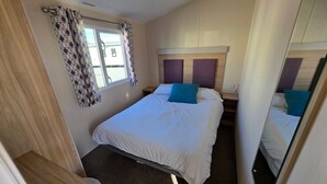 A bedroom with a bed, a window with curtains, a headboard, and a mirror. - Seaview 1. (Skegness)
