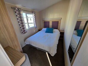 Ein Schlafzimmer mit Bett, Vorhängen am Fenster, Kopfteil und Spiegel.