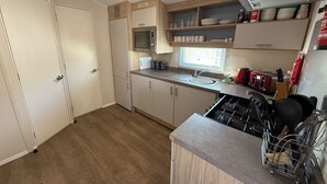A compact kitchen with a built-in microwave, a sink, and a gas stove. There are cabinets and a window providing natural light. - Seaview 1. (Skegness)