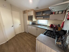 Eine kompakte Küche mit integriertem Mikrowellenherd, Spüle und Gaskochfeld. Schränke und ein Fenster sorgen für natürliches Licht.