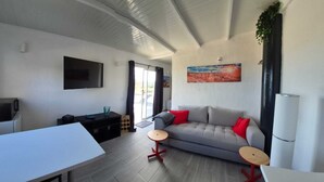 Una sala de estar moderna con un sofá gris, cojines rojos, un televisor de pantalla plana, una mesa de comedor y una mesita de madera.