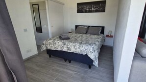 Un dormitorio con cama, mesita de noche, lámpara y un cuadro de paisaje urbano en la pared.