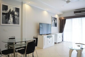 Ein modernes Wohnzimmer mit einem Glastisch, schwarzen Stühlen, einem Flachbildfernseher und einem weißen Schrank.