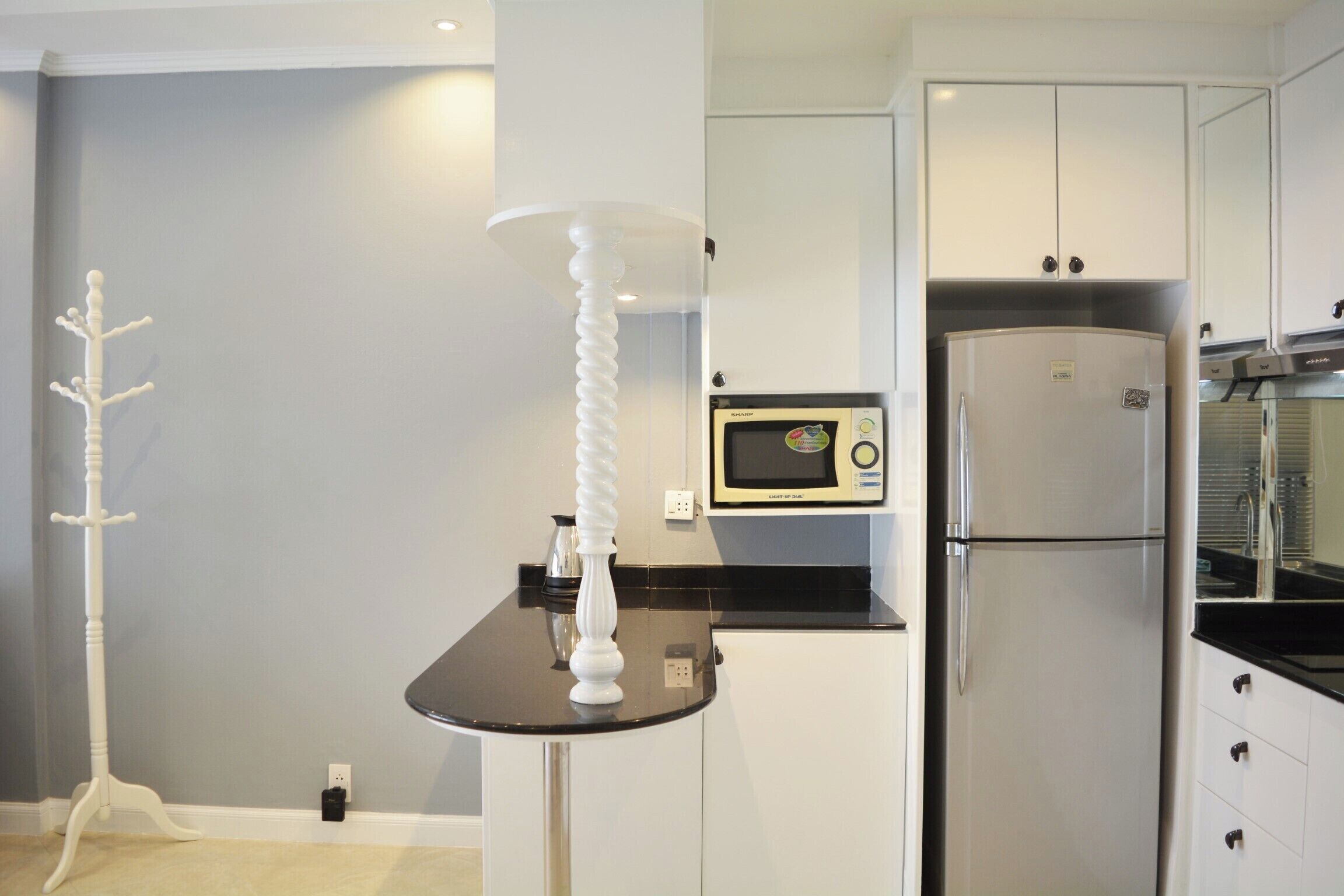 A compact kitchen with white cabinets, a black countertop, a microwave, and a stainless steel refrigerator.