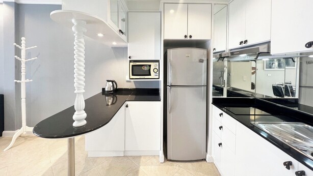 A modern kitchen with white cabinets, a black countertop, a stainless steel refrigerator, and a microwave. - Modern Pool-view 1-bedroom Condo With Large Balcony - Baan Suan Jomtien (Pattaya)