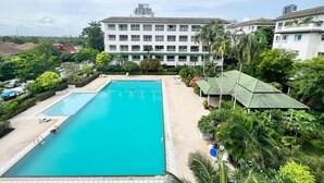 A large rectangular pool with a clear blue water, surrounded by lush greenery and a multi-story building with balconies in the background. - Modern Pool-view 1-bedroom Condo With Large Balcony - Baan Suan Jomtien (Pattaya)