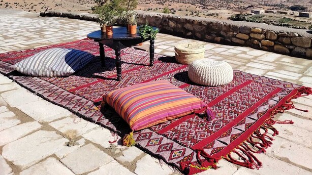 A terrace with a patterned rug, cushions, a small table with potted plants, and a view of a mountainous landscape. - Casa Marmoucha View Steppes de l'Atlas Yoga Retreat 11 pers (Aichoune)