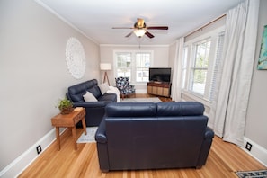 A living room with a dark blue sofa, a wooden side table with a plant, a ceiling fan, and a TV on a stand.
