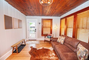 Une pièce avec un plafond en bois, un canapé en cuir marron, un tapis en peau de vache, un banc et une porte avec une fenêtre.