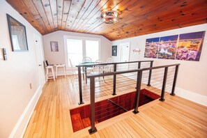A room with a wooden ceiling, a dining area with chairs, a table, and a staircase with a metal railing.