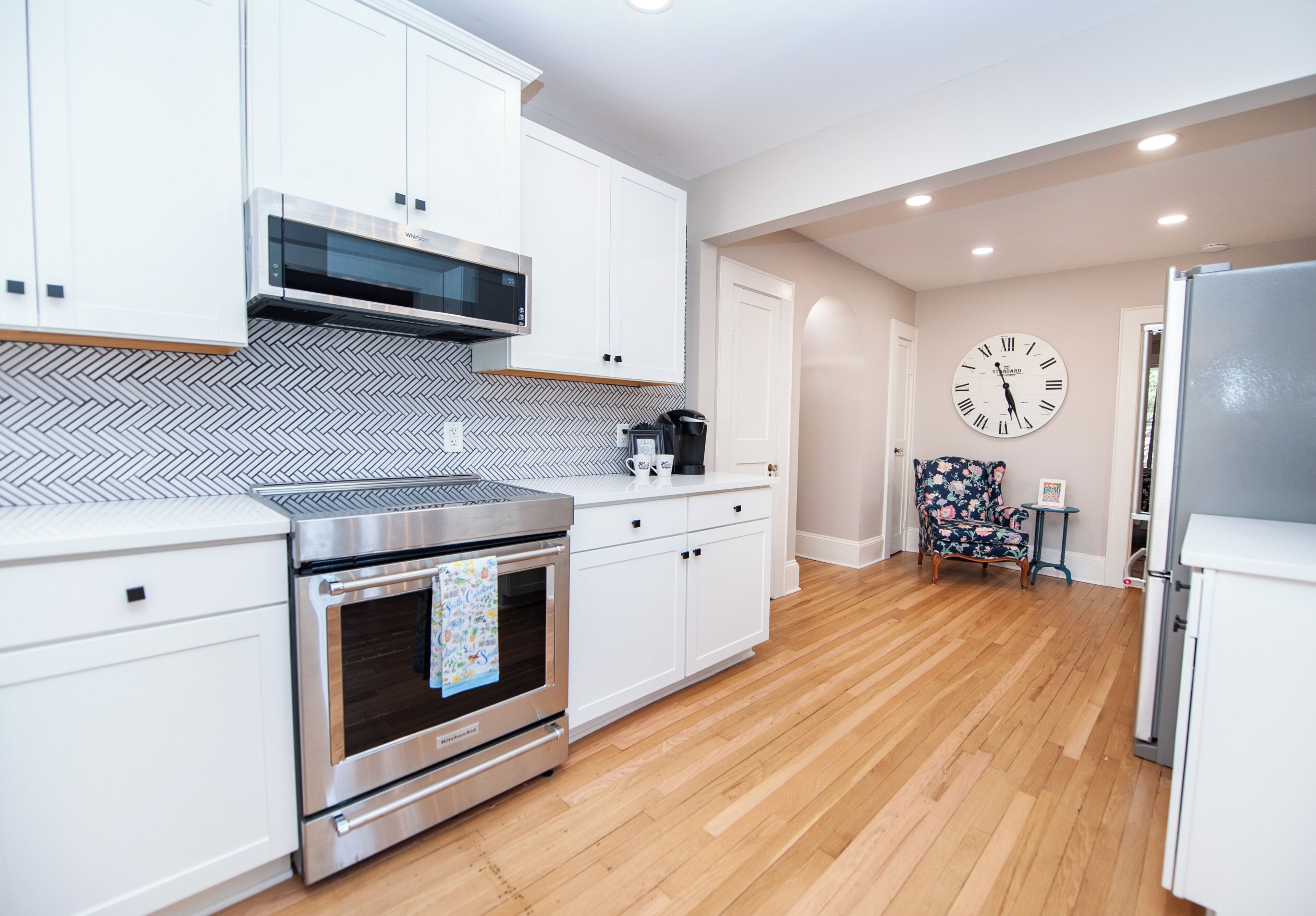 Una cocina moderna con armarios blancos, un horno de acero inoxidable, un microondas y un reloj en la pared.