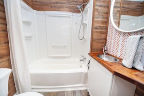 Une salle de bain avec une baignoire blanche, un meuble-lavabo en bois, un lavabo et un miroir.