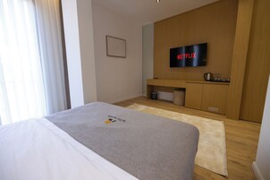 Habitación de hotel con una cama, un televisor montado en la pared, un armario de madera y un cesto de basura pequeño.