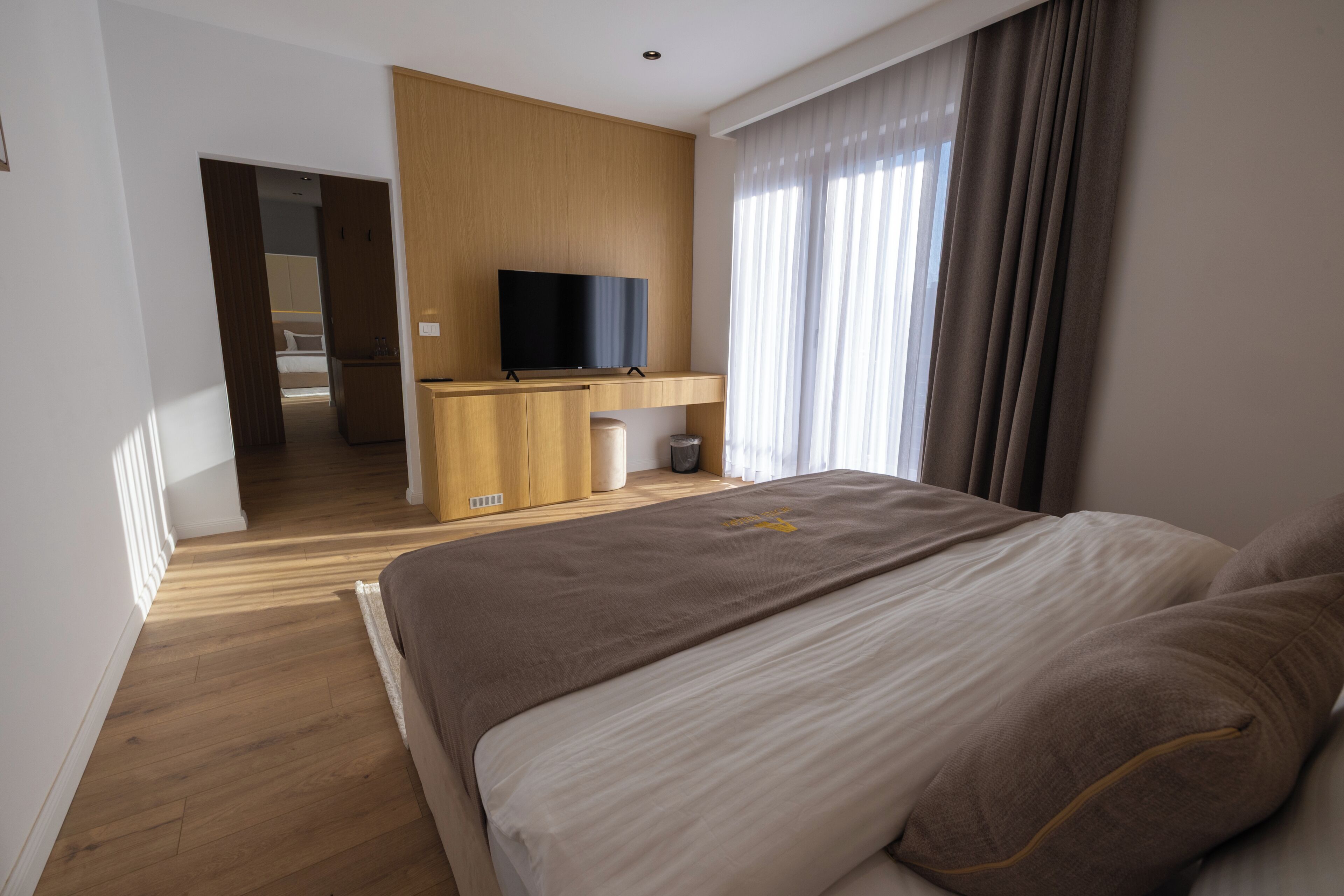 A modern hotel room with a large bed, a TV on a wooden console, and a view of a balcony.
