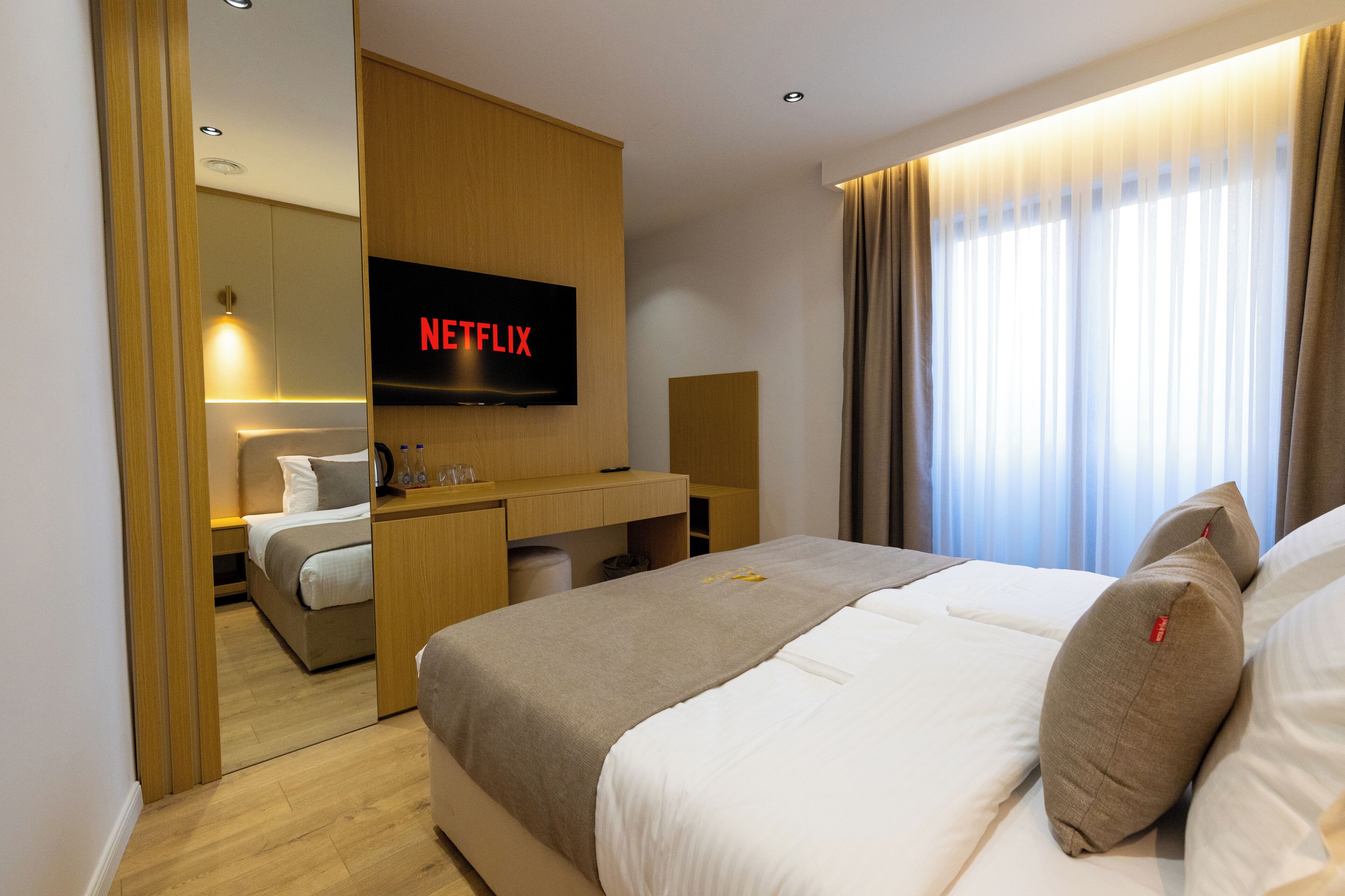 Una habitación de hotel con cama, escritorio, televisor y ventana con cortinas.