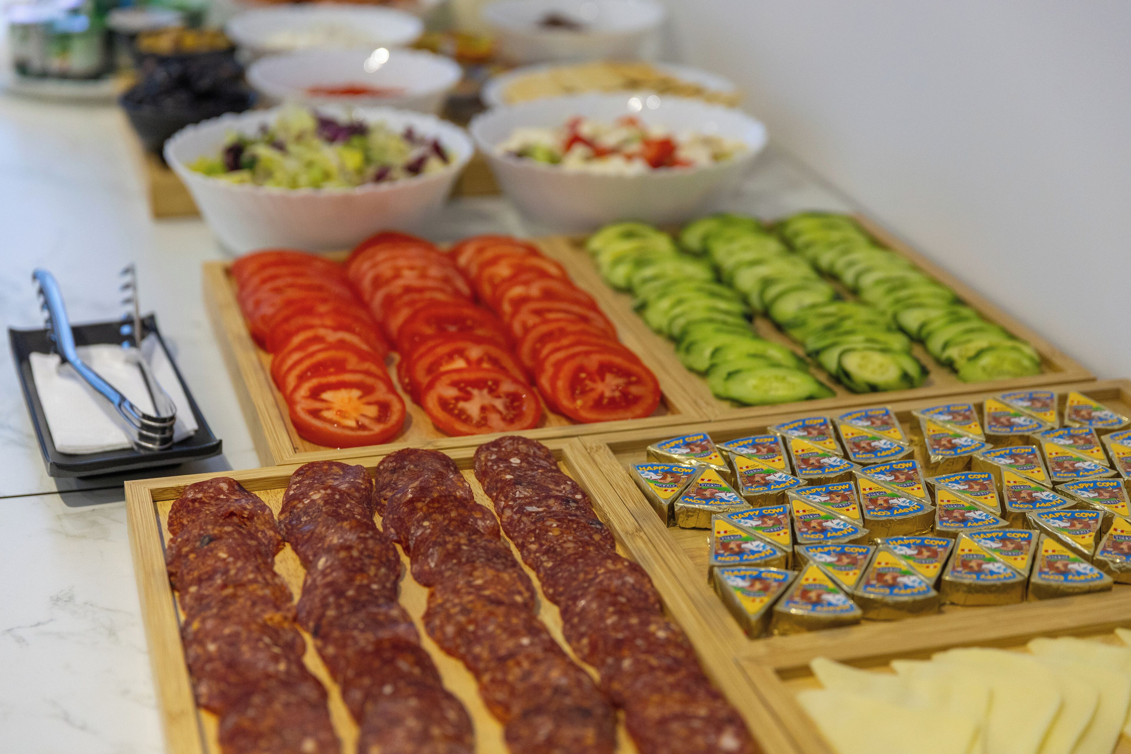 A buffet with sliced tomatoes, cucumbers, and various cheeses.