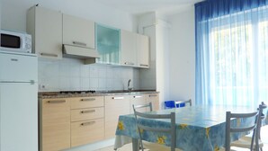 Cocina compacta con microondas, estufa y armarios. Hay una mesa de comedor con sillas y una ventana con cortinas azules.