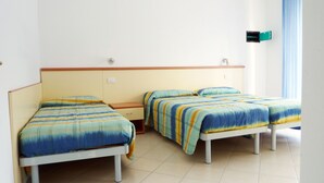 Una habitación con tres camas individuales, cada una con cubrecama a rayas. Hay una mesita de noche de madera entre las camas y una ventana con cortinas azules al lado derecho.