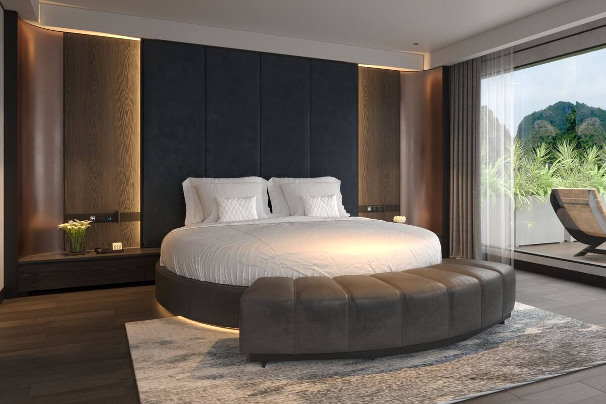 A modern bedroom with a large bed, a curved bench, and a view of greenery through a large window.