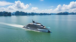 En stor, moderne yacht sejler på rolige farvande med frodige grønne øer i baggrunden.