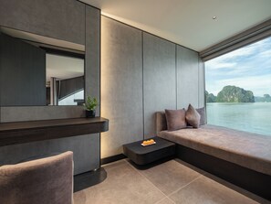 A modern interior with a large window, a built-in bench, and a small table with a plant and fruit. - Victorious Cruise Halong Bay (Tuan Chau)